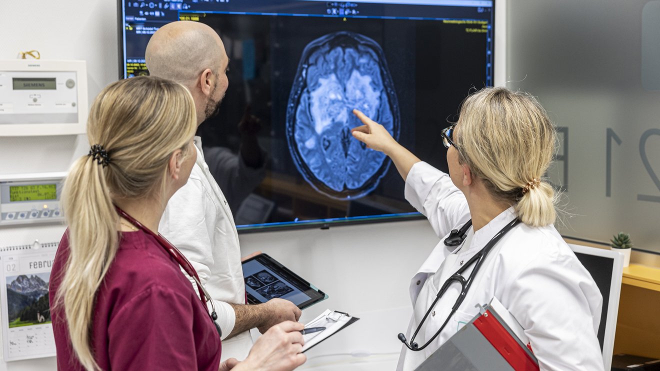 3 Ärzte begutachten Querschnittaufnahme eines Gehirns an einem Monitor